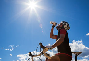 Cyclist resting and drinking water. Backlight, sunny summer day.