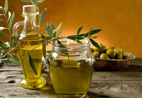 A jar of olive oil with fresh olives