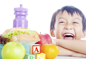 Boy with a lunch box filled with healthy food and "A-B-C" blocks nearby