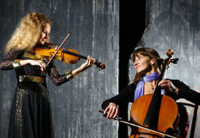 Daughter and mother playing on cello and violin on grey wall background