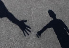 a shadow on pavement of an adult hand offering help to a child