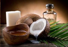 a coconut half, coconut oil in a coconut shell and an bottle of coconut oil on a palm leaf on a dark background