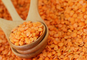 red lentils in a wooden spoon on a background of lentils