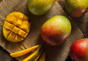 ripe mangos with one cut mango and mango slices on a wooden background