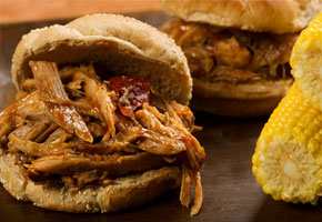 a pulled pork sandwich on a wooden board with an ear of corn