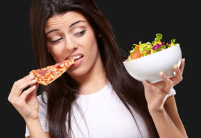 woman eating pizza while looking at a bowl of salad on a dark background