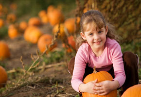 a pretty girl sitting in a pumpkin patch, hugging a pumpkin, with a fall background.