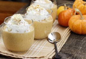 3 pumpkin yogurt parfaits in small glasses on a wooden table with a spoon and 3 small pumpkins