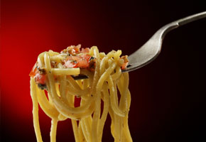 a fork lifting spaghetti with fresh tomatoes on a deep red background