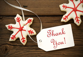 two sugar cookies decorated as snowflakes with a thank you tag and ribbon on a wooden background