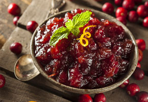 a bowl of homemade fresh cranberry-cherry compote on a wooden table with fresh cranberries all around