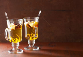 2 mugs containing warm cider with pear and lemon peel on a dark background
