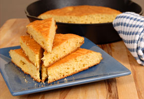 a skillet containing cornbread in the background, with a blue plate of wedges of cornbread in the foreground
