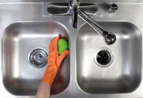 a stainless steel sink begin cleaned by a gloved hand