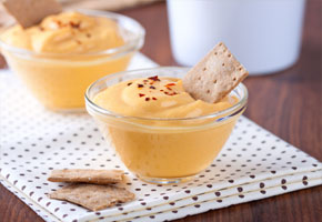 pumpkin dip in a clear glass cup with a graham cracker for dipping on a wooden table