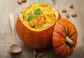 a fresh pumpkin filled with pumpkin risotto and fresh sage on a wooden table with a wooden spoon