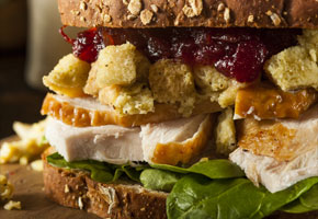 a close up of a sandwich filled with thanksgiving leftovers like cranberry sauce, stuffing and turkey