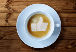 steaming cup of coffee with a thumbs up symbol in the foam on a wooden background