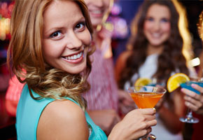 pretty dark haired girl holding a holiday cocktail in foreground with party-goers in the background