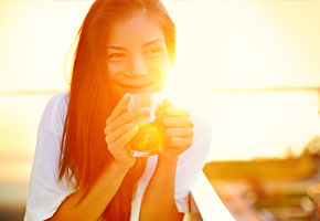 beautiful asian woman drinking hot beverage with the sun behind her
