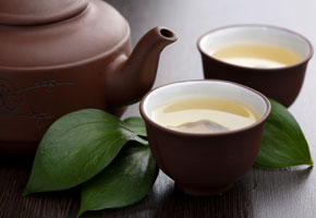 a pot of green tea with two cups of green tea on a wooden table
