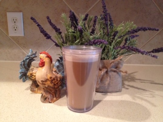 a coconut oil latte in a tall glass surrounded by lavendar plants on a light colored kitchen countertop