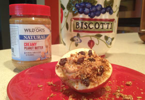 An apple stuffed with peanut butter, raisins and granola on a red plate