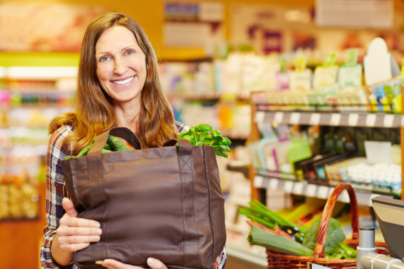 Smiling woman holding full shopping bag with vegetables in organ