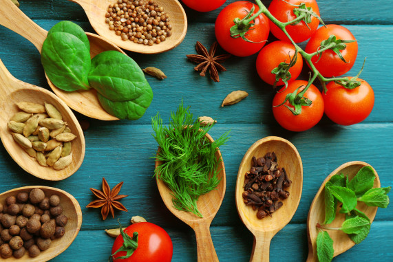 Tomatoes with wooden spoons with fresh herbs and spices on wooden background